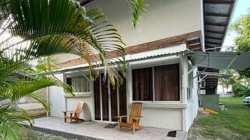 Ein Haus mit verdeckter Veranda, zwei Holzstühlen und einer Palme.