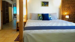 A hotel room with a large bed, a wooden headboard, a painting on the wall, and a view of the hallway. - Gardenview Retreat | Beachfront | Walk Everywhere (Manzanillo)