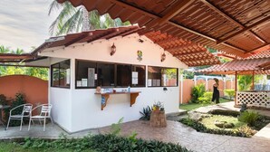 A covered outdoor seating area with a white building, a wooden counter, and a small garden. - La Casita Beachfront Hideaway | Pool Access (Manzanillo)