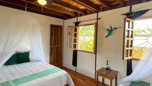 A room with two beds, wooden flooring, a ceiling fan, and a window with a view of greenery. - Tropical Vibe Home | Pool | Walk to Beach & Dining (Manzanillo)