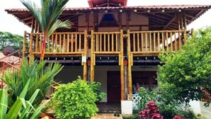 A two-story wooden building with a balcony, surrounded by lush greenery and potted plants. - Seaside Escape | Entire House | Pool Access (Manzanillo)
