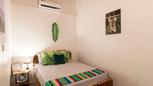 A bedroom with a bed, a nightstand with a lamp, a wall-mounted air conditioner, and a framed picture. - Poolside | 2BR Home | Walk to Beach & Dining (Manzanillo)