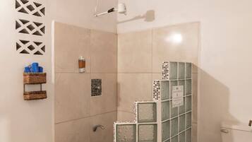 Ein Badezimmer mit Dusche, geflieste Wände, Toilette und einem kleinen Mülleimer.