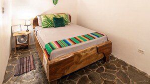 A bedroom with a wooden bed, a nightstand with a lamp, a fan, and a wall-mounted plant. - Poolside | Beach Access | Walk to Dining (Manzanillo)
