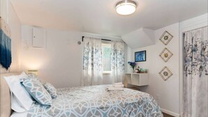 Ein Schlafzimmer mit Bett, Vorhängen am Fenster, Nachttisch mit Lampe und Wanddekorationen.
