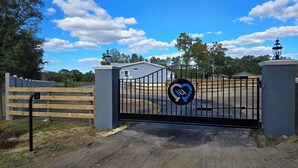 Une entrée fermée par un portail, ornée d’un logo bleu et blanc, une clôture en bois et un bâtiment visible au loin.