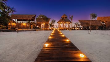 Un sendero de madera que conduce a un complejo turístico frente a la playa con construcciones de techo de paja.