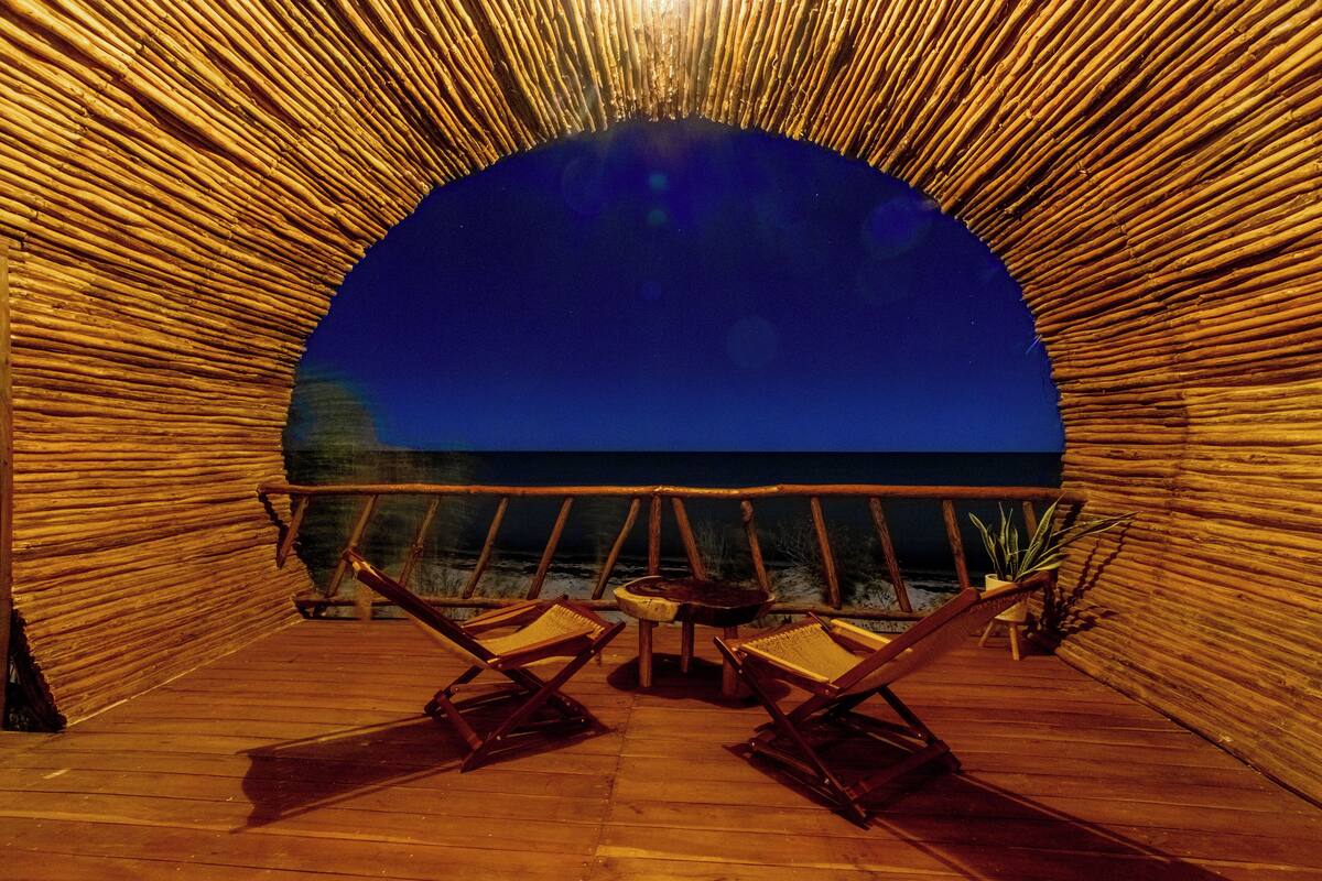 A wooden deck with a semi-circular bamboo structure, two wooden chairs, and a small table.