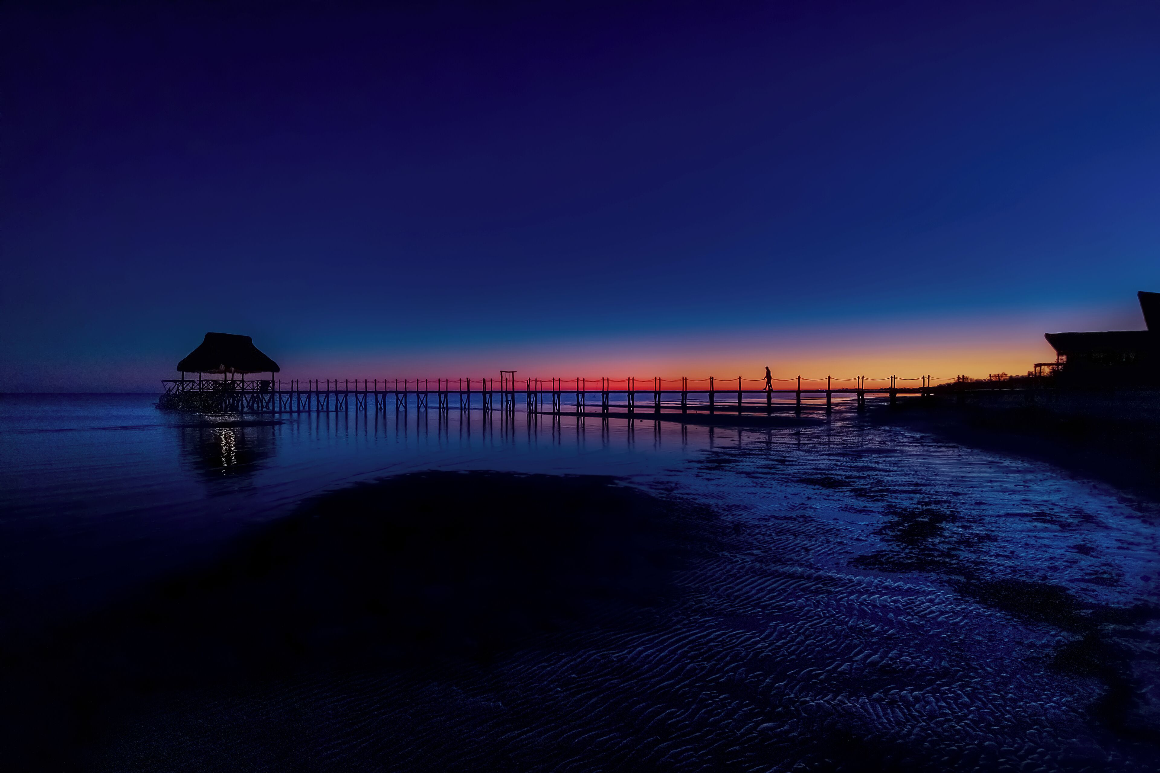 A pier extending into calm waters at dusk with a small structure on one end.