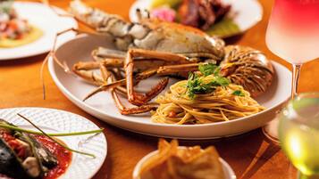 Een eettafel met diverse gerechten, waaronder zeevruchten, pasta en een glas witte wijn.