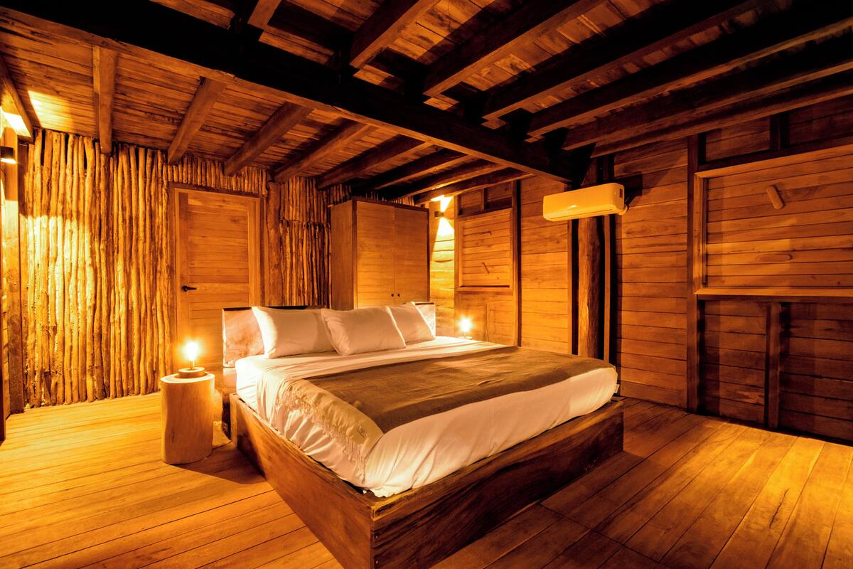 A wooden cabin-style bedroom with a large bed, wooden walls, and a sloped ceiling.