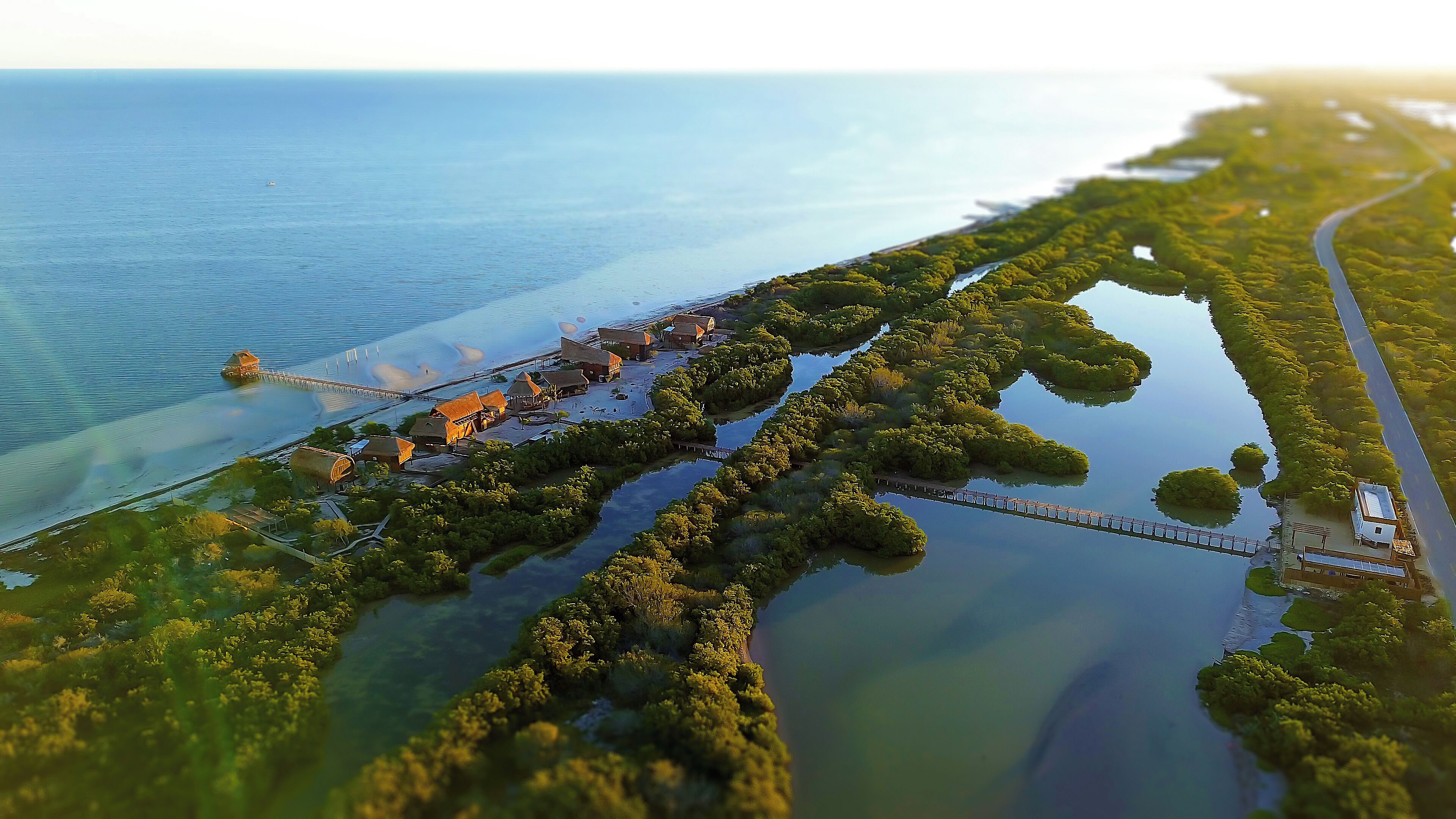 Eine Vogelperspektive eines Küstenresorts mit mehreren Gebäuden, einem Steg und einer Brücke, die das Land mit dem Wasser verbindet.