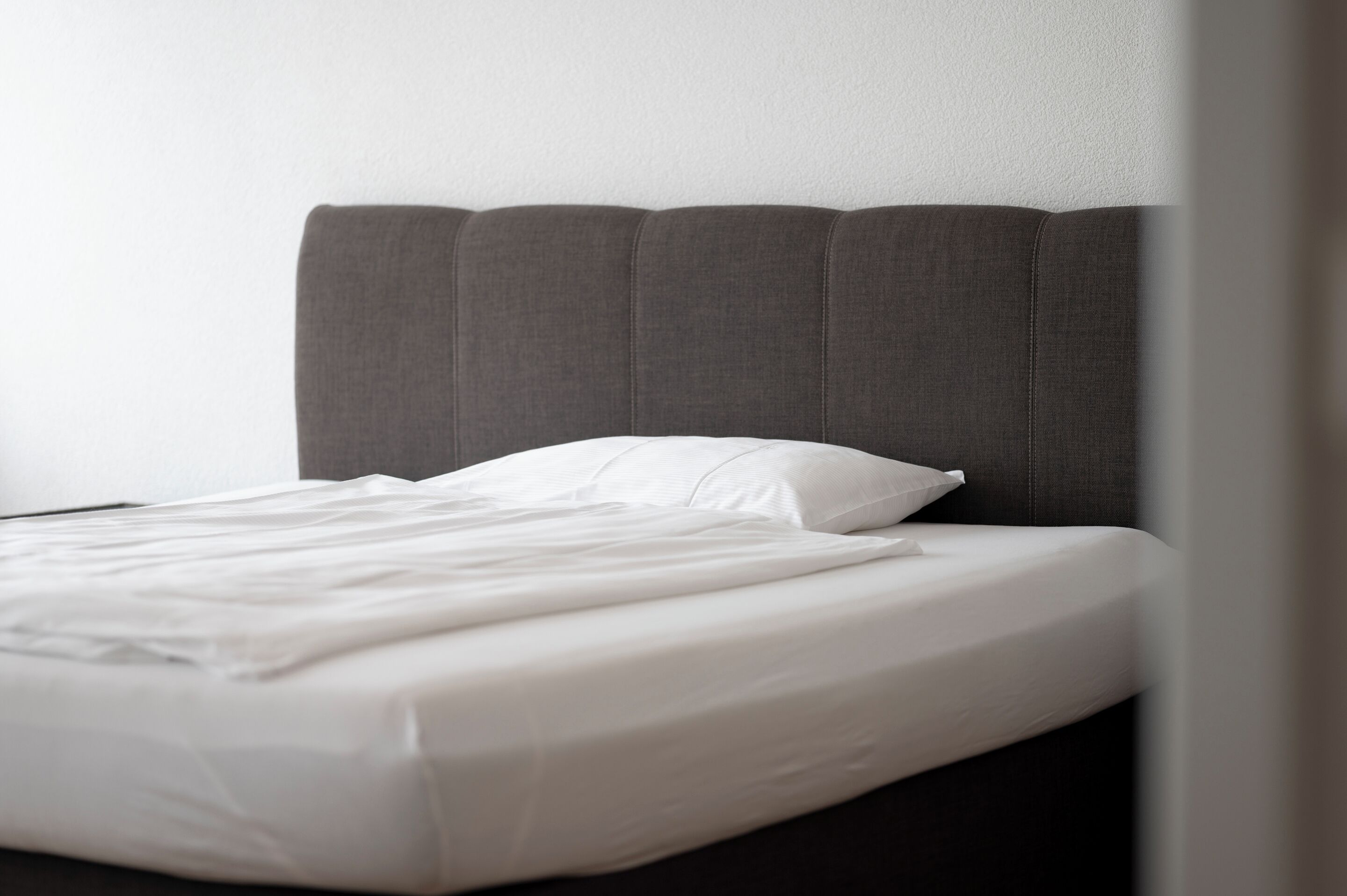 Un lit bien fait, avec du linge de lit blanc et une tête de lit sombre.