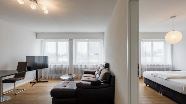 Una habitación moderna con sofá modular, televisor de pantalla plana, mesa de comedor y cama.