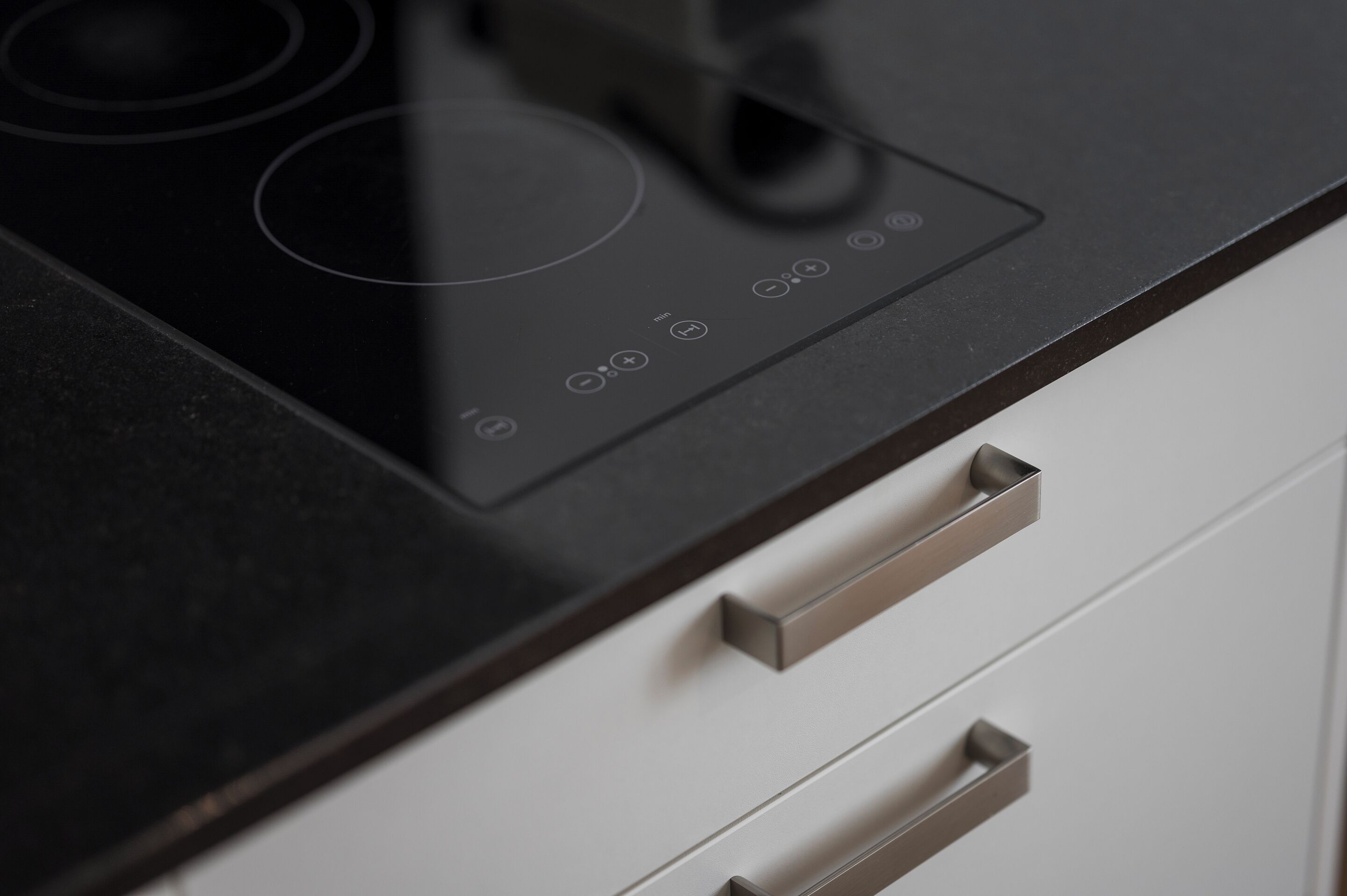 Una cocina con tope de inducción negro y dos pomos de acero inoxidable en un armario blanco.