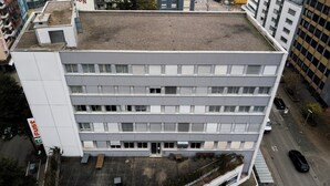 Un edificio de varios pisos con techo plano, ventanas grandes y un estacionamiento al frente.