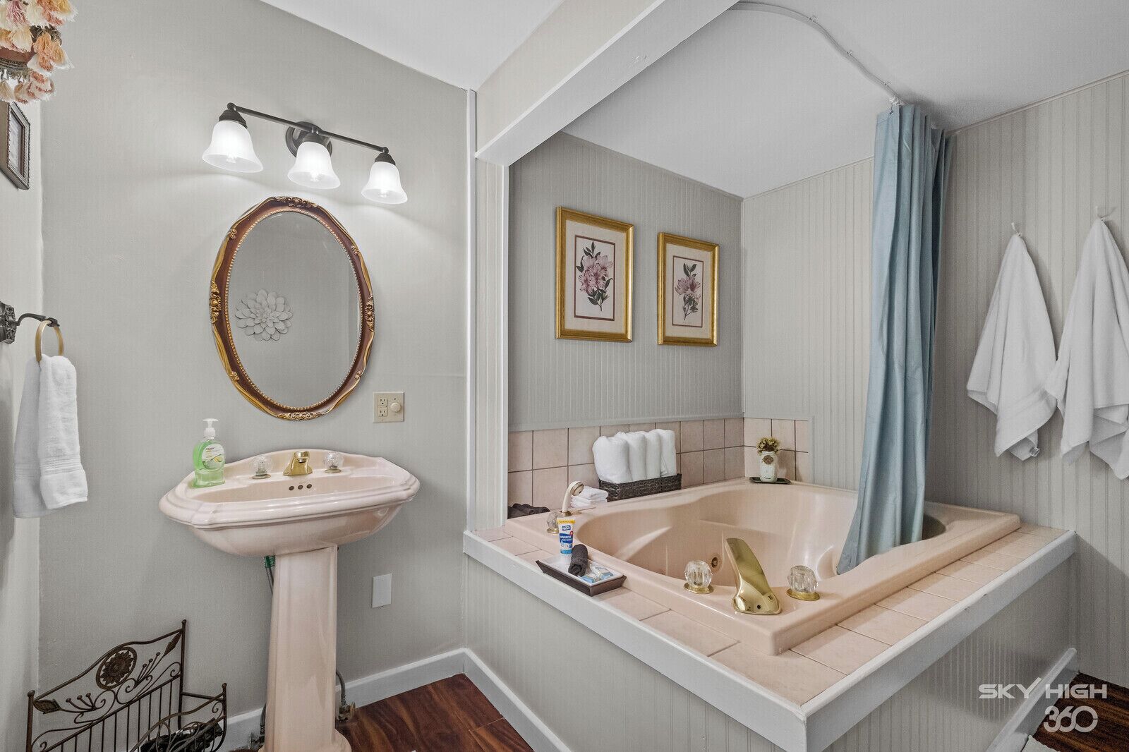 A bathroom with a pedestal sink, a large mirror, a bathtub, and a shower curtain.