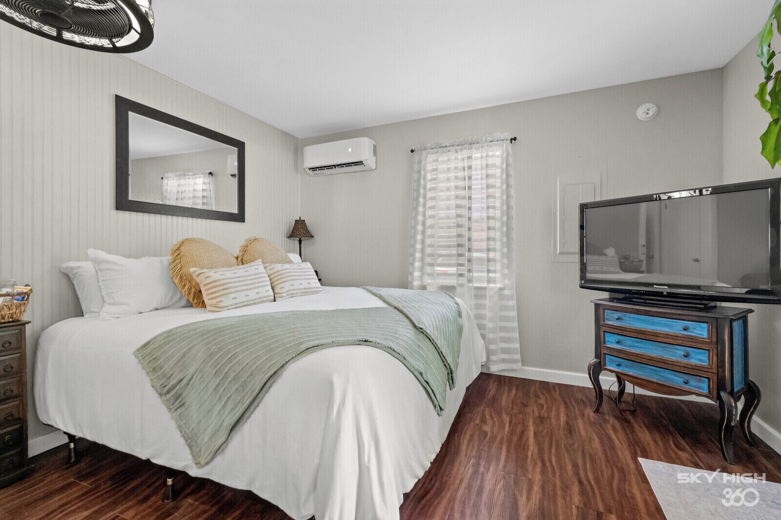 A bedroom with a bed, a television, a dresser, and an air conditioning unit.