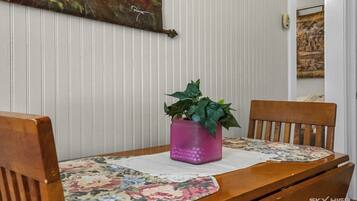 A dining table with a floral placemat, two wooden chairs, and a potted plant in a pink vase.