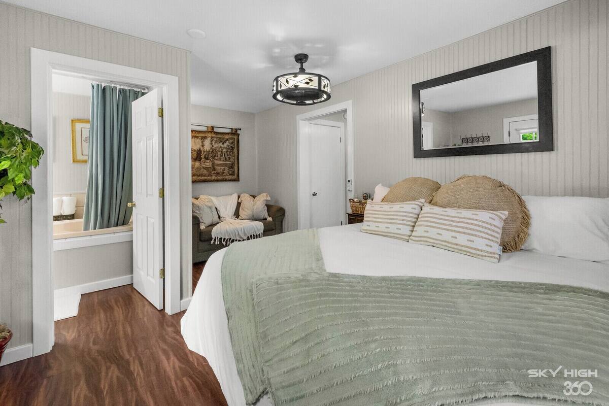 A bedroom with a large bed, a mirror, a ceiling fan, and a door leading to a bathroom.