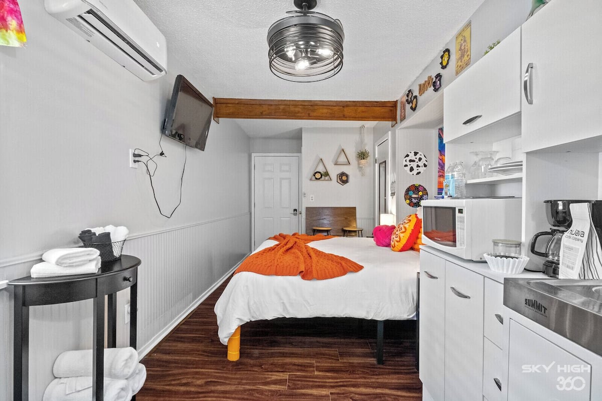 A compact bedroom with a bed, bedside table, and a small desk with a chair.