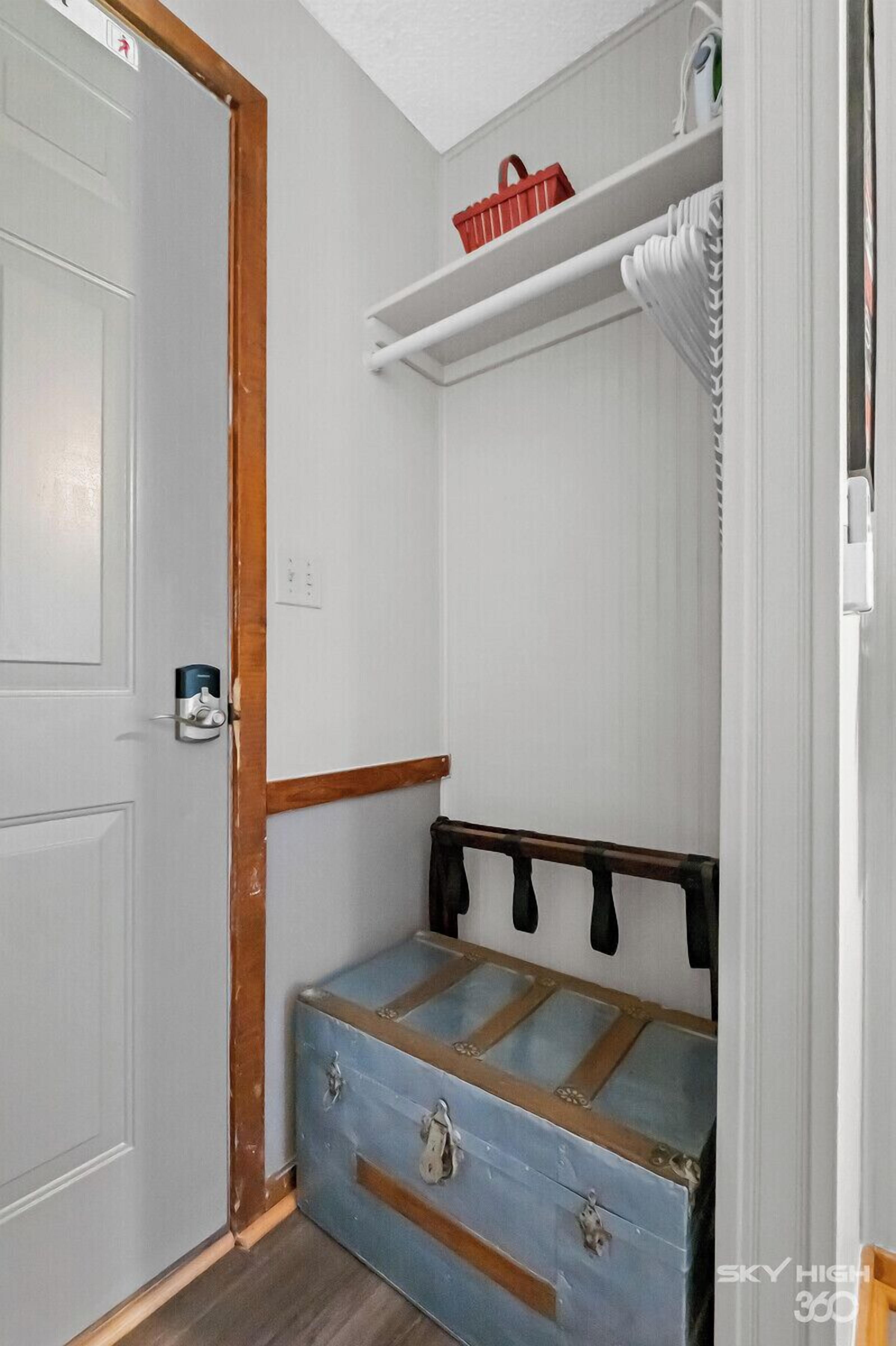 A small room with a wooden door, a blue chest of drawers, a white shelf with a red basket, and a white radiator.