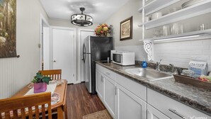Una cocina compacta con armarios blancos, encimera de granito, microondas, refrigerador y lavabo.