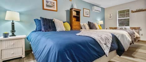 A bedroom with a large bed, wooden headboard, and a ceiling fan. There is a nightstand with a lamp and a small plant.