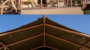 Een bamboestructuur met twee verdiepingen en een overdekt balkon, dat schaduw biedt en uitzicht geeft op de omgeving.