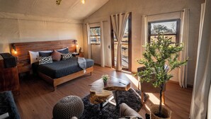 Un dormitorio con una cama de madera, una mesita, una planta en maceta y vistas al exterior.