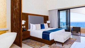 Een moderne hotelkamer met een groot bed, een zithoek en een balkon met uitzicht op de oceaan.