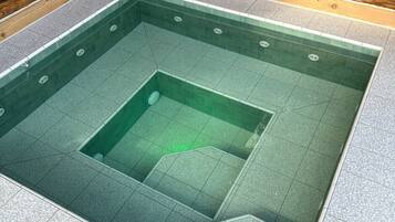 A square hot tub with a central drain, surrounded by a tiled floor with a pebble pattern.