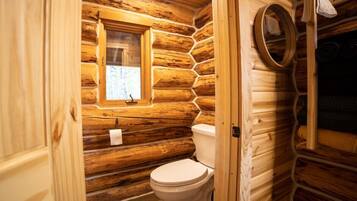 Un baño de cabaña de troncos con interior de madera, un inodoro, una ventana y un espejo.