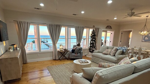 A spacious living room with a large window overlooking the sea, a cozy sofa set, and a Christmas tree. - “Beach’d Pearl” Beach house with Private Beach and Pier in Ocean Springs (Ocean Springs)