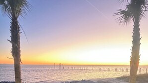 A beach view with palm trees, a sandy area, and a wooden deck. - “Beach’d Pearl” Beach house with Private Beach and Pier in Ocean Springs (Ocean Springs)