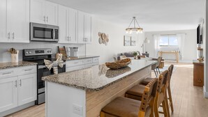 A modern kitchen with white cabinets, a granite countertop, a microwave, and a large island with bar stools. - NEW! Tide's End Getaway (Panama City Beach)