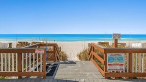 A wooden boardwalk leading to a beach with clear blue water, a caution sign, and a rip current warning sign. - NEW! Tide's End Getaway (Panama City Beach)