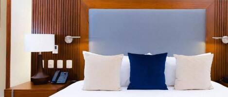 A hotel room with a large bed, a bedside table with a lamp, and a phone.