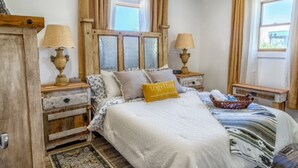 Un dormitorio con cama, dos mesitas de noche, un armario de madera y una ventana con cortinas.