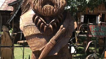 A wooden sculpture of a bearded man holding a stick, surrounded by rustic buildings and greenery.