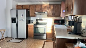 A kitchen with wooden cabinets, stainless steel appliances, a refrigerator, oven, microwave, and a coffee maker.