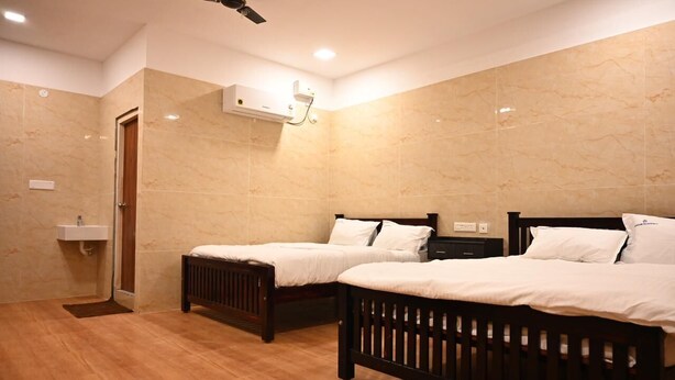A hotel room with two wooden beds, a ceiling fan, a built-in air conditioning unit, and a small bathroom with a sink. - Thangam Residency (Tiruvannamalai)