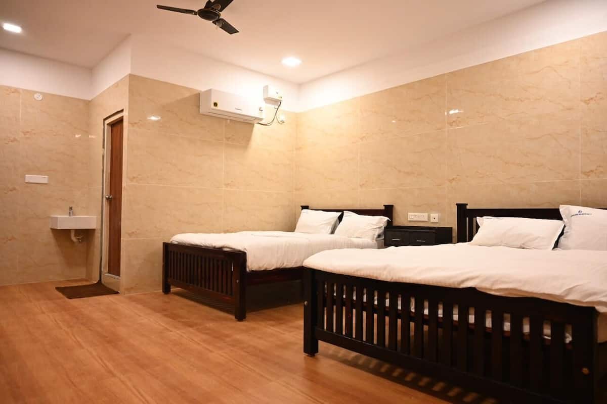 A hotel room with two wooden beds, a ceiling fan, a built-in air conditioning unit, and a small bathroom with a sink.