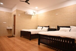 Hotelkamer met twee houten bedden, een plafondventilator, een ingebouwde airconditioning en een kleine badkamer met een wastafel.