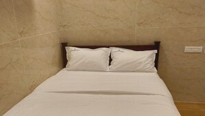 A neatly made bed with white bedding and wooden headboard in a room with marble walls. - Thangam Residency (Tiruvannamalai)