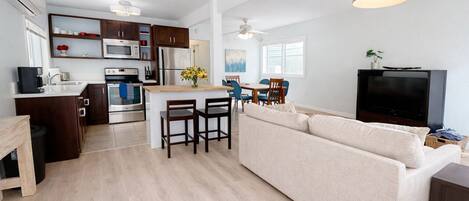A modern kitchen with a central island, dining area with chairs, a sofa, and a TV in a living room.