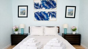 Habitación de hotel con una cama grande, dos mesitas de noche, vistas a las montañas y un cuadro con hojas tropicales en la pared.