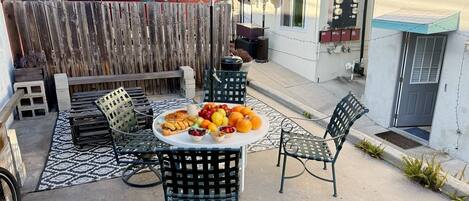 Un patio al aire libre con una mesa lista para comer, rodeado de sillas y un paraguas azul.