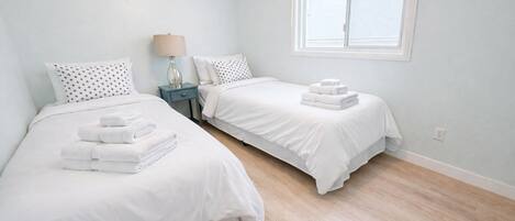 A bedroom with two beds, a nightstand with a lamp, and a window.