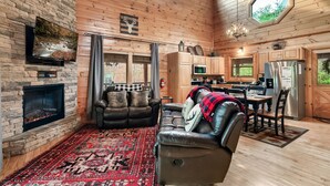 Un intérieur de chalet chaleureux avec une cheminée en pierre, des canapés en cuir, un coin repas et une cuisine.
